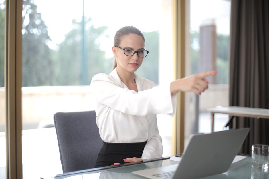 Concentrated businesswoman wearing formal clothes and eyeglasses pointing away while standing in office and working on project in laptop during work